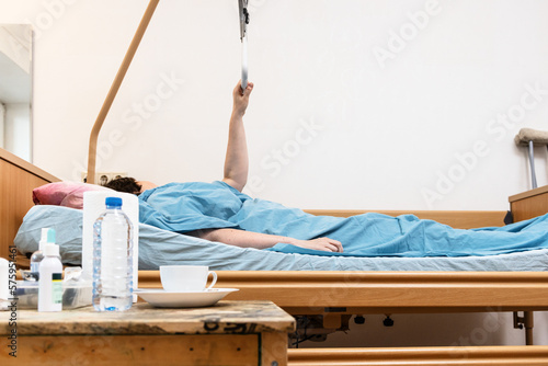 homecare adjustable electric hospital bed with sick person holding handle and table with medicine on foreground at home photo