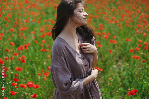Stylish sensual woman in rustic dress relaxing in red poppy field. Cottagecore aesthetics. Young female in linen dress enjoying summer among wildflowers meadow in sunny countryside, slow life © sonyachny