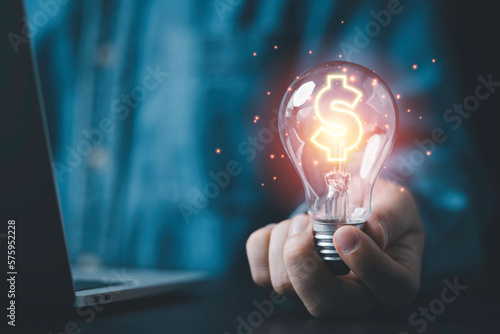Billede på lærred Businessman holding lightbulb and glowing dollar sign for creative thinking idea and problem solving can make more money concept