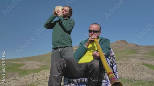 Guys play music on didgeridoo and sea shell. Friends are outdoors photo