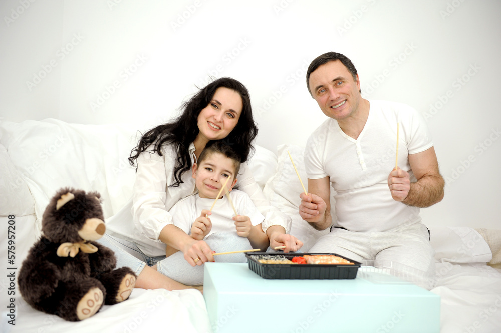 home delivery of sushi happy cheerful family in white clothes on bed eating sushi from disposable tableware with chopsticks toy teddy bear nearby european family happy eating bed day off spending time home delivery of sushi happy cheerful family in white clothes on bed eating sushi from disposable tableware with chopsticks toy teddy bear nearby european family happy eating bed day off spending time