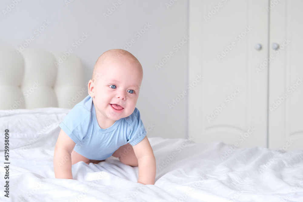 smiling boy with big blue eyes in a bodysuit learns to crawl on white bedding. Healthy newborn baby