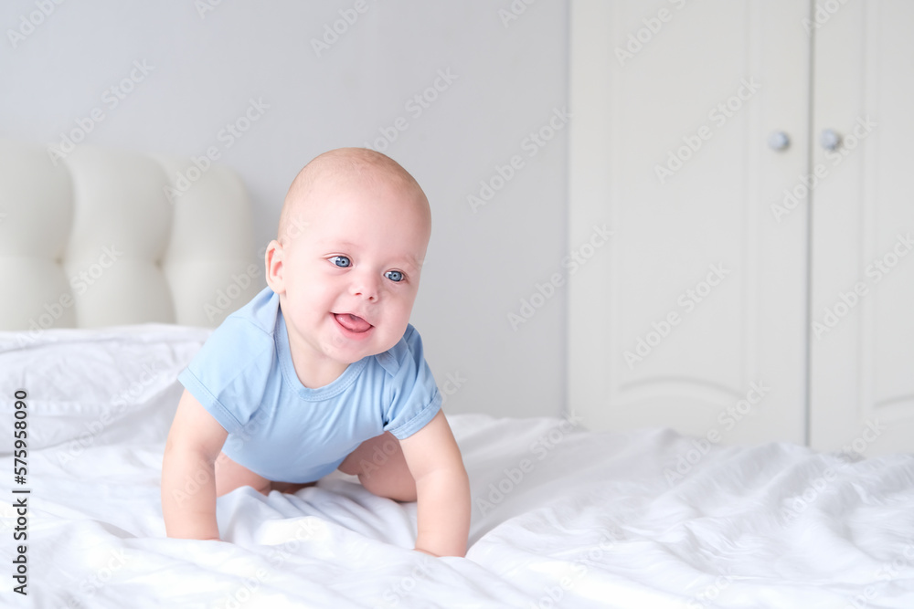 smiling boy with big blue eyes in a bodysuit learns to crawl on white bedding. Healthy newborn baby smiling boy with big blue eyes in a bodysuit learns to crawl on white bedding. Healthy newborn baby