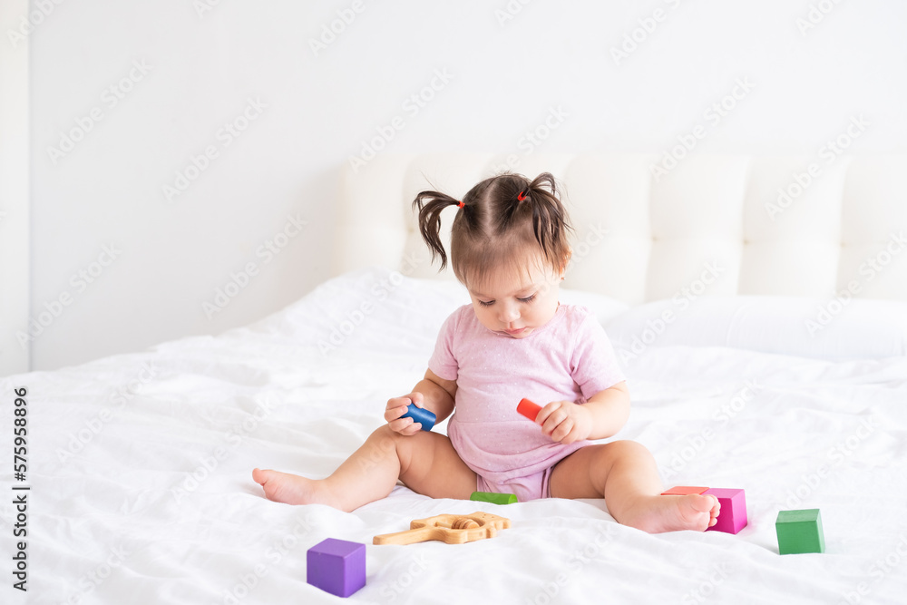 funny baby girl in pink bodysuit playing with children wooden cubes toys on bed funny baby girl in pink bodysuit playing with children wooden cubes toys on bed