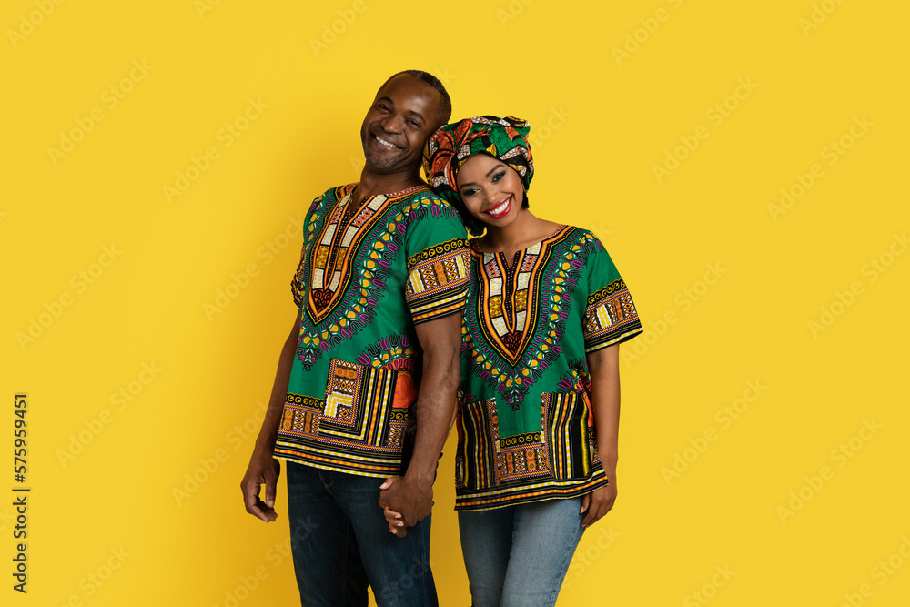 Cheery husband and wife in african costumes posing on yellow