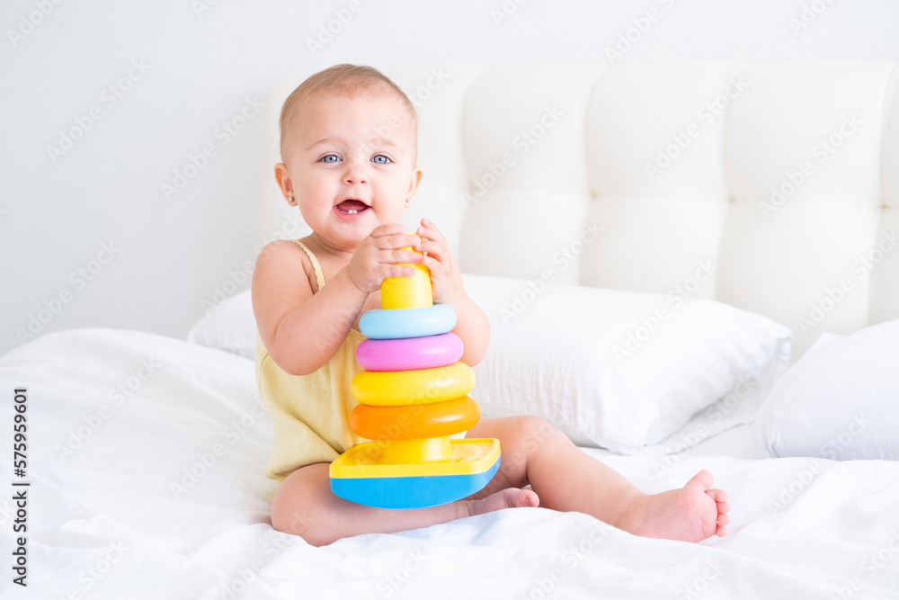 funny baby girl in yellow bodysuit playing with plastic toy children pyramid on bed funny baby girl in yellow bodysuit playing with plastic toy children pyramid on bed