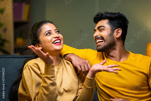 Fotografia Happy laughing young couple on sofa talking closely at home during weekend night