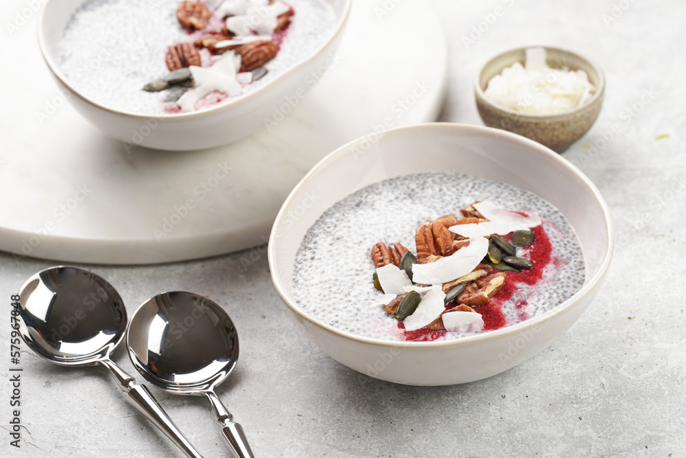 Breakfast idea - two bowls with with chia seeds pudding, red raspberry smoothie, pecan nuts, coconut flakes and pepitas on gray background Breakfast idea - two bowls with with chia seeds pudding, red raspberry smoothie, pecan nuts, coconut flakes and pepitas on gray background