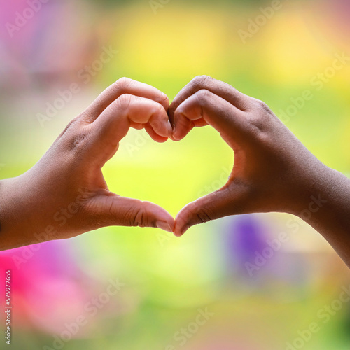 Kids hands making heart symbol with colourful background.