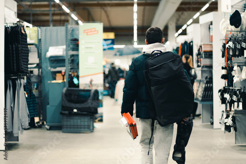 A young guy with a backpack walks down the aisle in the store.