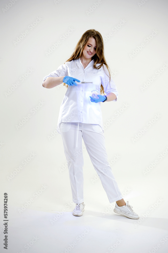 Photopolymer lamp Beautiful female doctor with a lamp in her hands smiling in a white suit on white background studio photo advertising dental office space for text banner billboard Photopolymer lamp Beautiful female doctor with a lamp in her hands smiling in a white suit on white background studio photo advertising dental office space for text banner billboard