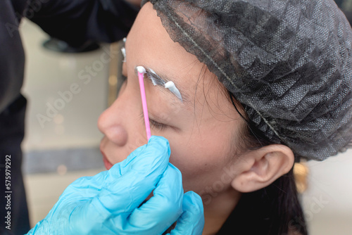 Obraz na plátne An esthetician applies numbing cream or topical anesthesia to a clients eyebrows prior to a microblading procedure