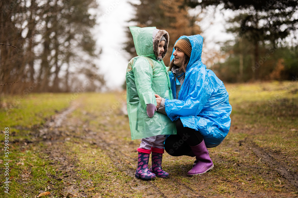 Fototapeta premium Mother with daughter in the forest after rain in raincoats together.