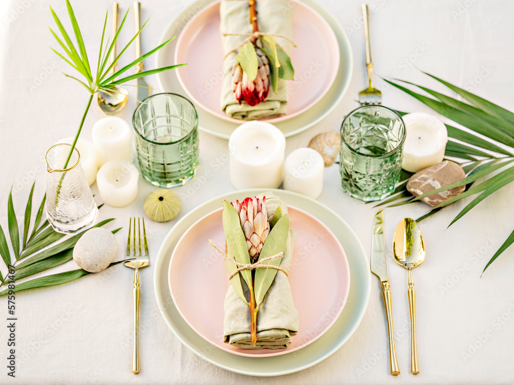 A beautiful floral table arrangement. Pastel crockery and golden cutlery make a luxury setting. The  composition of flowers and candles create a romantic atmosphere, perfect for a date or a wedding. - obrazy, fototapety, plakaty 