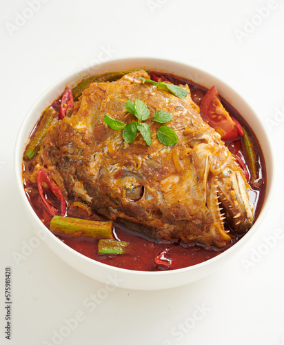Curry fish head with lady's finger and tomatoes in a wok. A malaysia cuisine with Indian influence. Top view isolated on white background