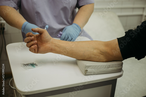 arm to elbow, preparation for taking blood for laboratory testing. In the background, the silhouette of a nurse in medical gloves