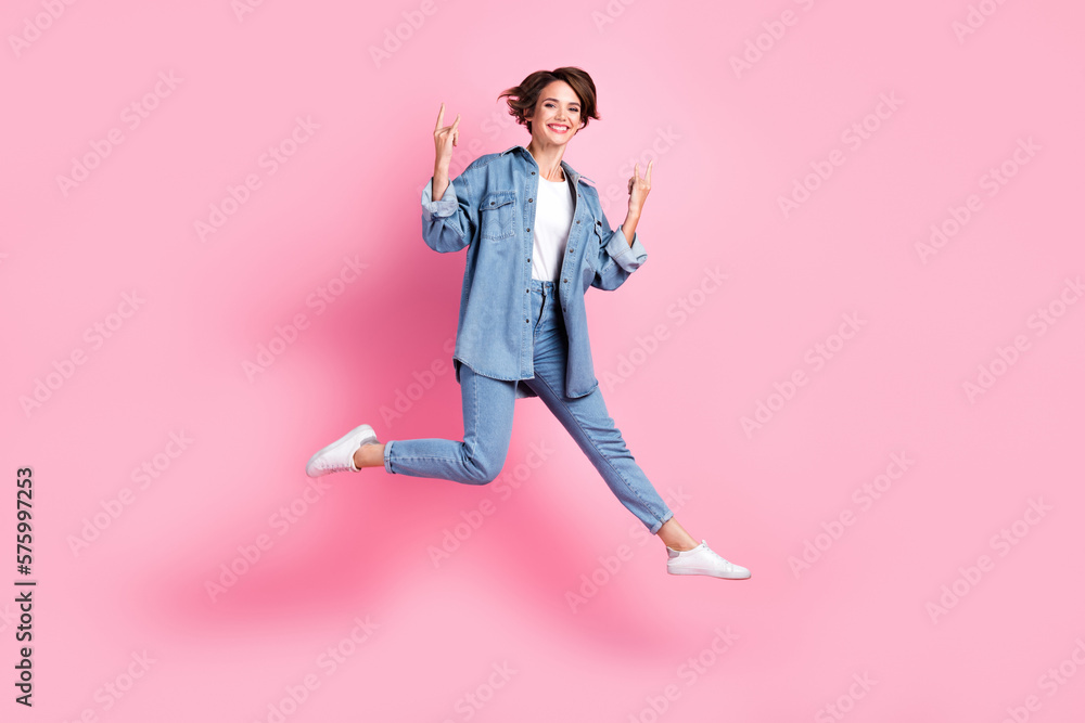 Full length photo of cool funky lady dressed denim jacket jumping high showing hard rock signs isolated pink color background