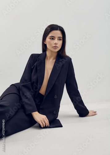 a beautiful woman poses relaxed sitting in a black suit on a light background