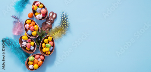Easter banner eggs hunt concept with flat lay chocolate eggs and bunny on blue background with copy space