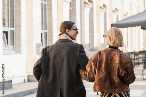 blonde woman in trendy leather jacket walking with happy and tattooed boyfriend on street.