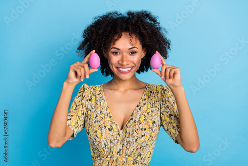 Photo of sweet shiny woman wear print dress rising two pink easter eggs isolated blue color background
