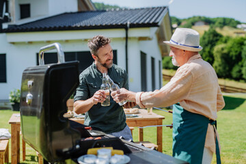Senior father with adult son grilling outside on backyard in summer during family garden party.