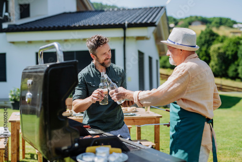 Senior father with adult son grilling outside on backyard in summer during family garden party.