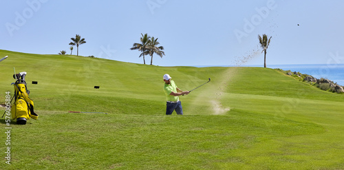 The golf player hits the ball from the bunker with a golf club, on a sunny day in summer.