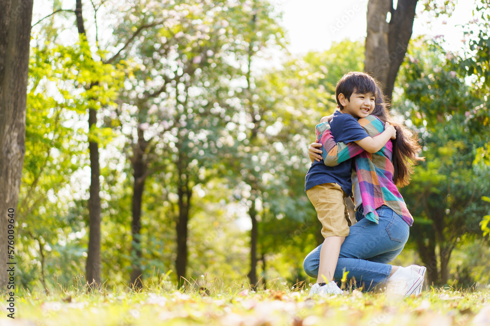 Asian little cute boy running to hug his mother at the park, mother and sun relaxation activity in a park or garden in weekend. Woman and a boy playing on a beautiful sunlight and bokeh background. Asian little cute boy running to hug his mother at the park, mother and sun relaxation activity in a park or garden in weekend. Woman and a boy playing on a beautiful sunlight and bokeh background.
