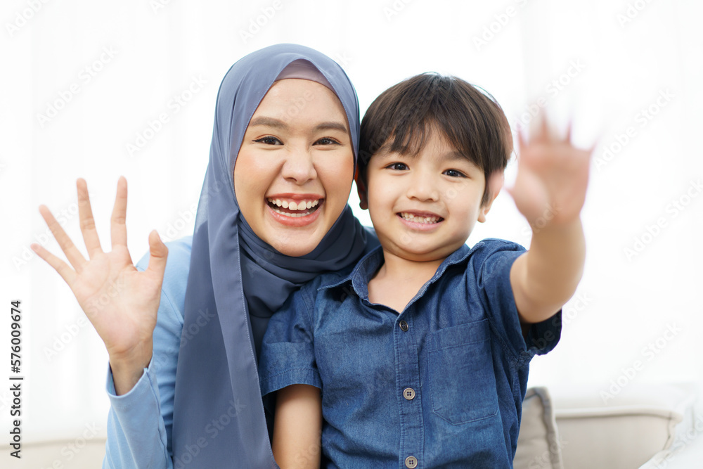 Happy cheerful Asian muslim family stay together in living room in weekend, Beautiful Asian woman muslim and lovely little boy portrait and looking at camera.