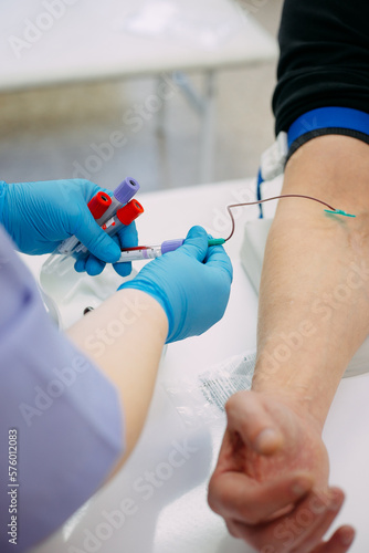 Close-up of a doctor's hands in blue gloves taking blood through a needle from a man's hand.