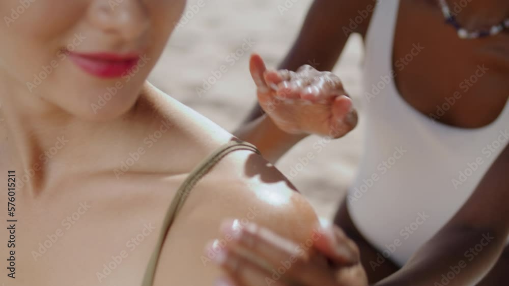 Closeup hands applying suntan cream on shoulder. Multiethnic girlfriends sunbath Closeup hands applying suntan cream on shoulder. Multiethnic girlfriends sunbath