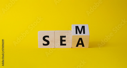 SEM vs SEA symbol. Turned wooden cubes with words SEA and SEM. Beautiful yellow background. Business and SEM vs SEA concept. Copy space