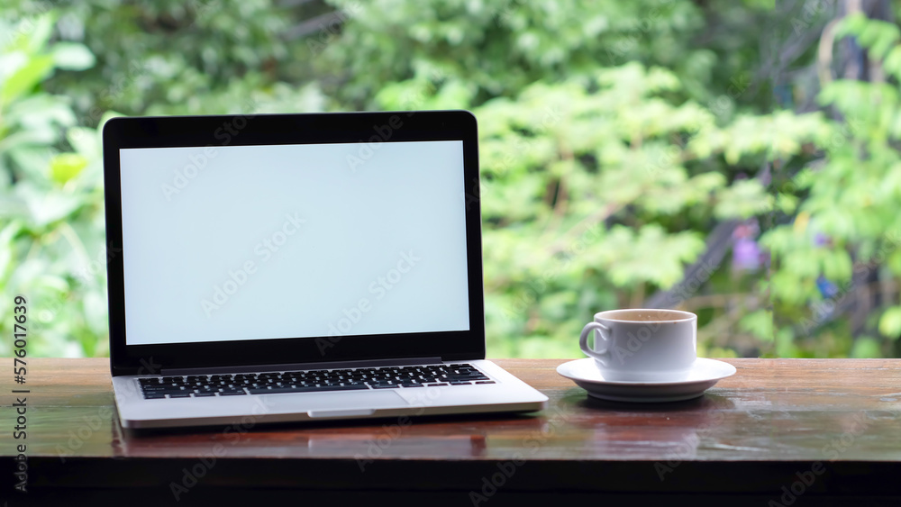 laptop with white screen and a coffee in white cup on the table garden view laptop with white screen and a coffee in white cup on the table garden view