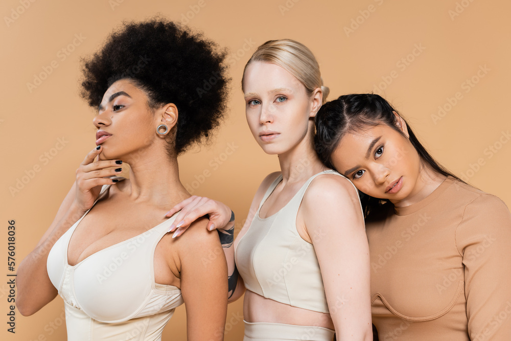 young interracial models in underwear looking at camera near curly african american woman isolated on beige. young interracial models in underwear looking at camera near curly african american woman isolated on beige.