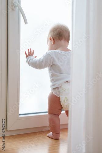 BabyToddler is standing with his hand on the window and looking at the street.