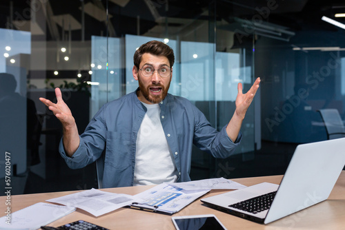 Photographie Portrait of disgruntled financier businessman inside office, male angry boss looking at camera and shouting displeased with report and paid bills, man doing paperwork inside office with laptop