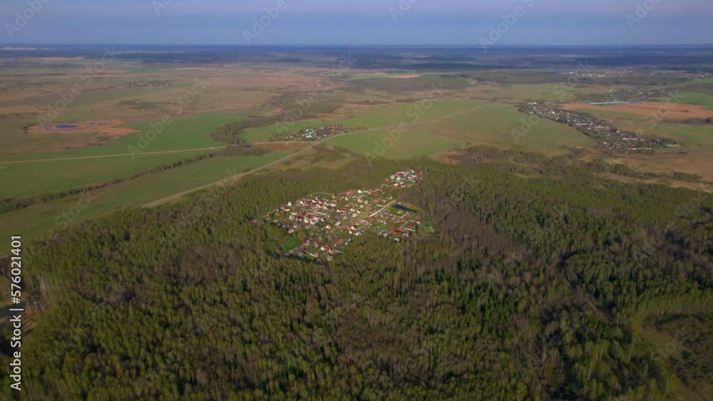 Village in middle of the forest. View from a flying drone of a small village in a forest surrounded by hilly fields against a blue sky. The concept of living in nature in ecologically clean places. Village in middle of the forest. View from a flying drone of a small village in a forest surrounded by hilly fields against a blue sky. The concept of living in nature in ecologically clean places.
