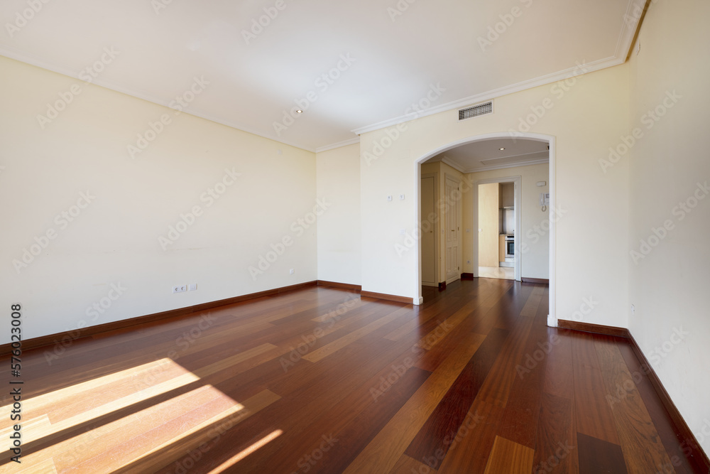 Empty room of a house with dark wooden floors and baseboards of the same tone with doorless access to the room with an arch from the hall Empty room of a house with dark wooden floors and baseboards of the same tone with doorless access to the room with an arch from the hall