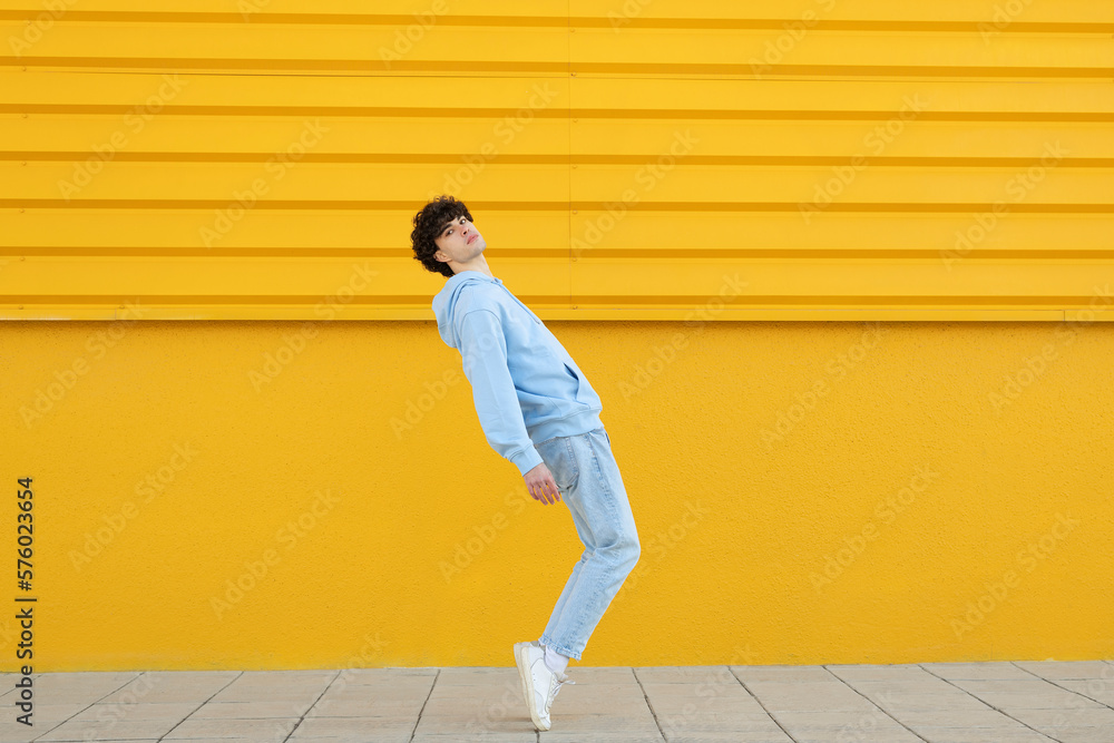 Man tiptoeing by yellow wall on footpath Man tiptoeing by yellow wall on footpath