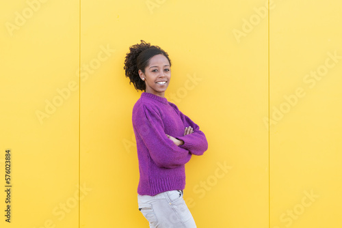 Happy woman with arms crossed standing by yellow wall photo