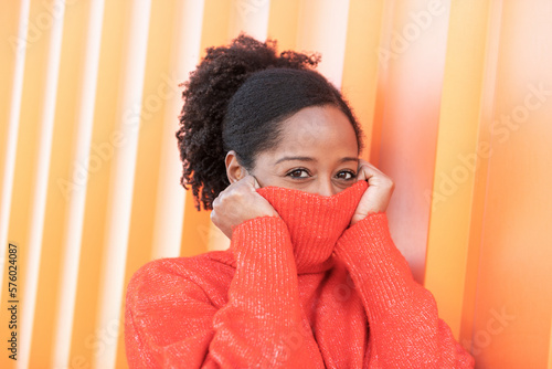Woman covering face with turtleneck sweater by orange wall photo