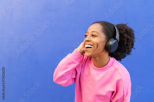 Happy woman listening to music through headphones in front of blue wall photo