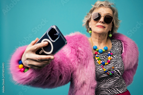 Smiling senior vlogger talking selfie using smart phone against turquoise background photo