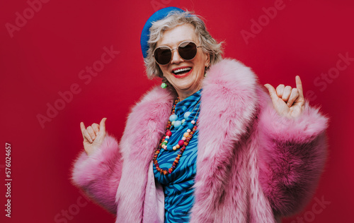 Happy senior woman wearing pink fur coat gesturing against red background photo