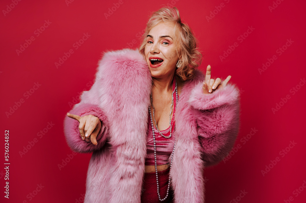 Senior woman with fur coat having fun against red background Senior woman with fur coat having fun against red background