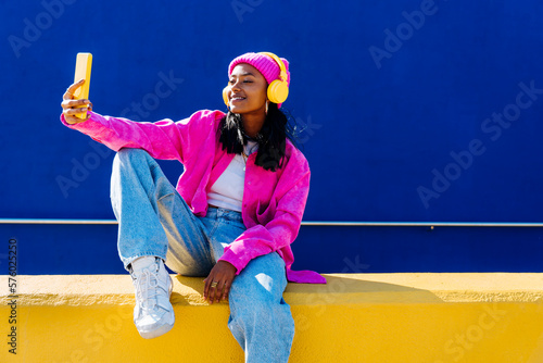 Smiling woman taking selfie through smart phone sitting on wall photo