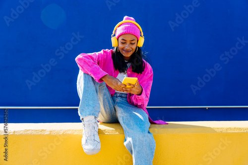 Smiling woman with headphones using smart phone on wall