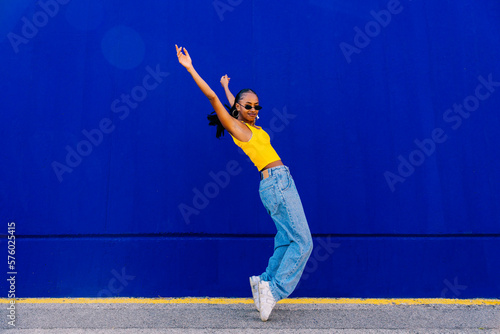 Young woman on tiptoes with arms raised by blue wall photo