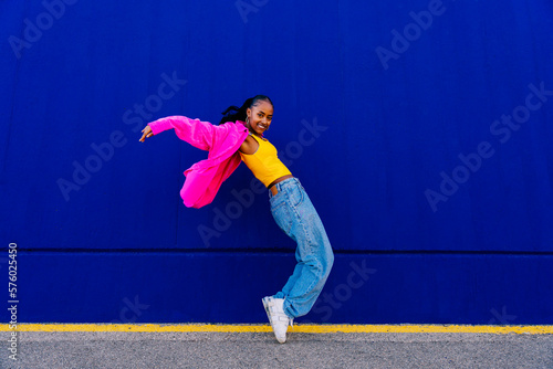 Happy woman dancing on tiptoe by blue wall